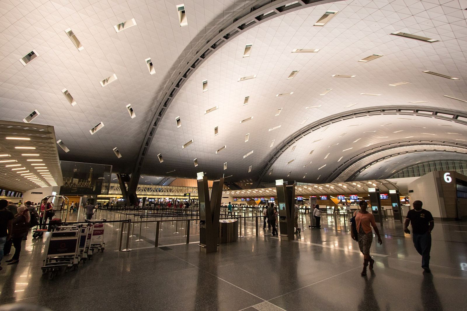 Departure hall at Hamad International Airport, Doha, under a sweeping curved roof with scattered skylights